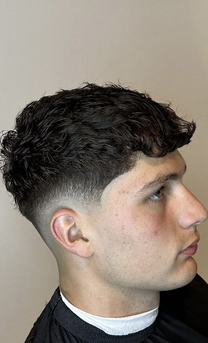 Textured curly top with low taper fade by Sharp Society Barbershop