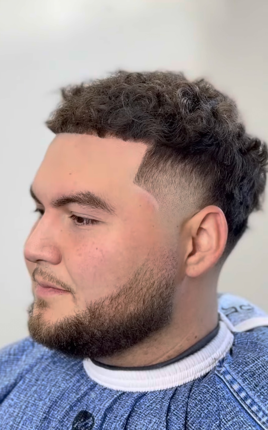 Curly top with low taper fade and beard by Sharp Society Barbershop