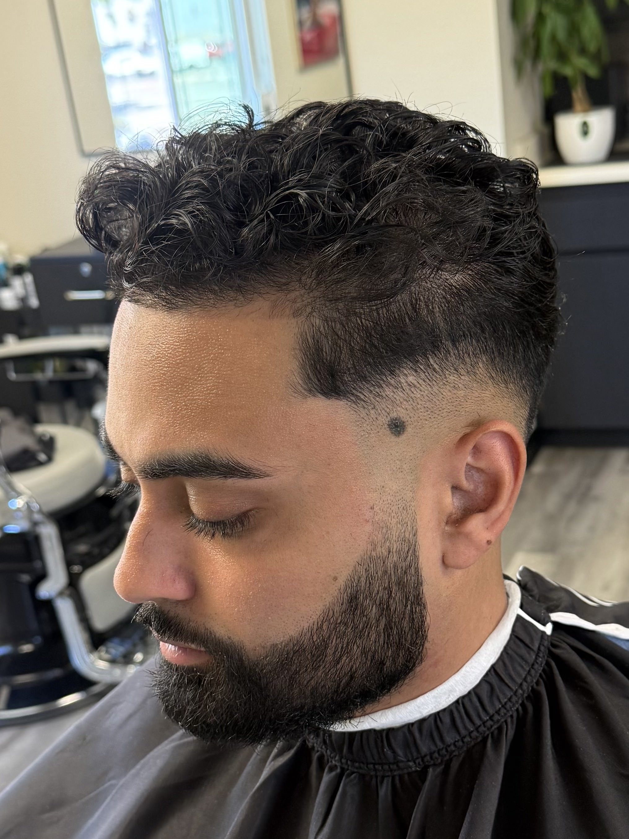Curly top with low taper fade and beard lineup by Sharp Society Barbershop